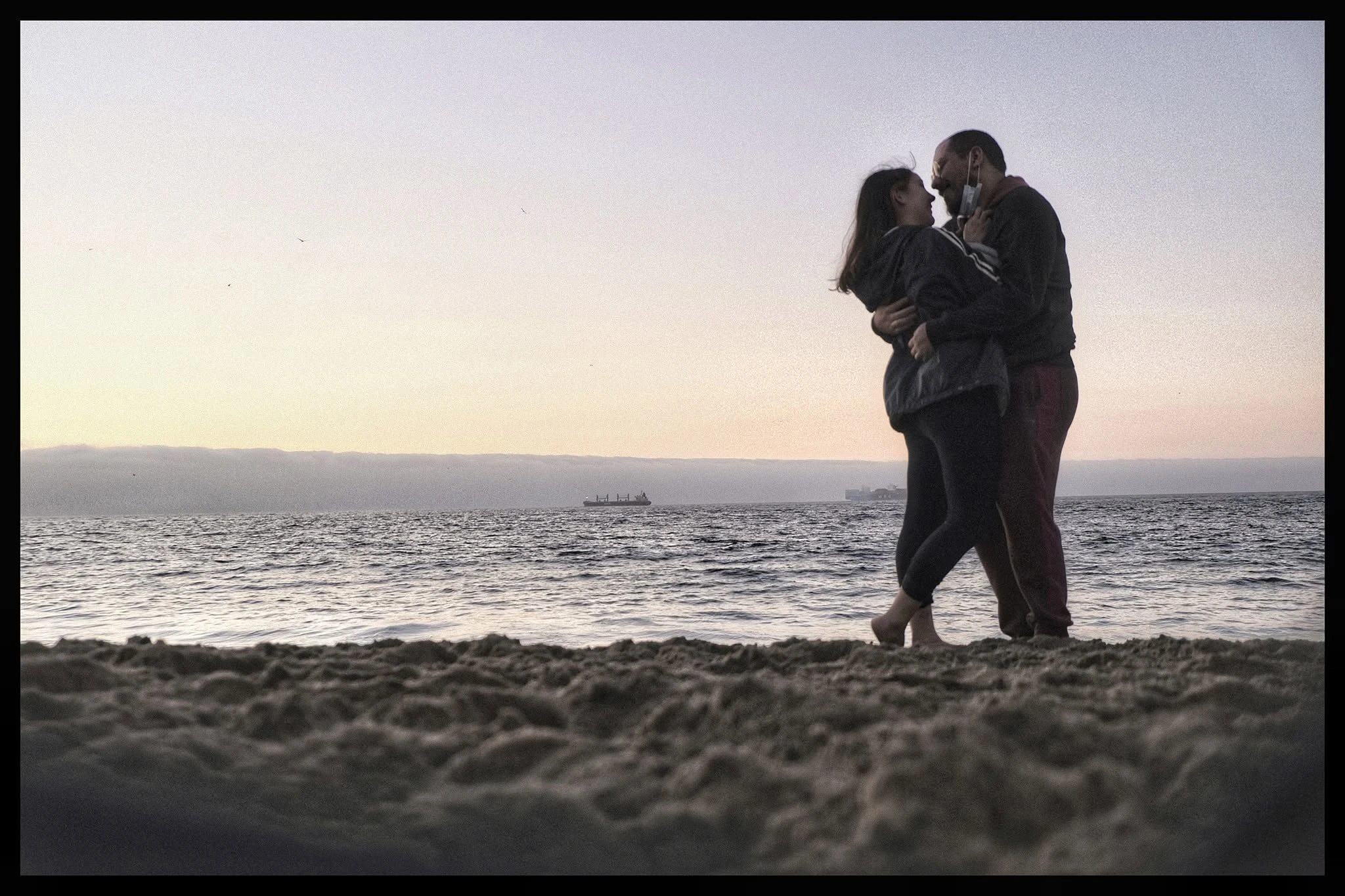 Josefa y Gabriel abrazados junto al mar al atardecer.